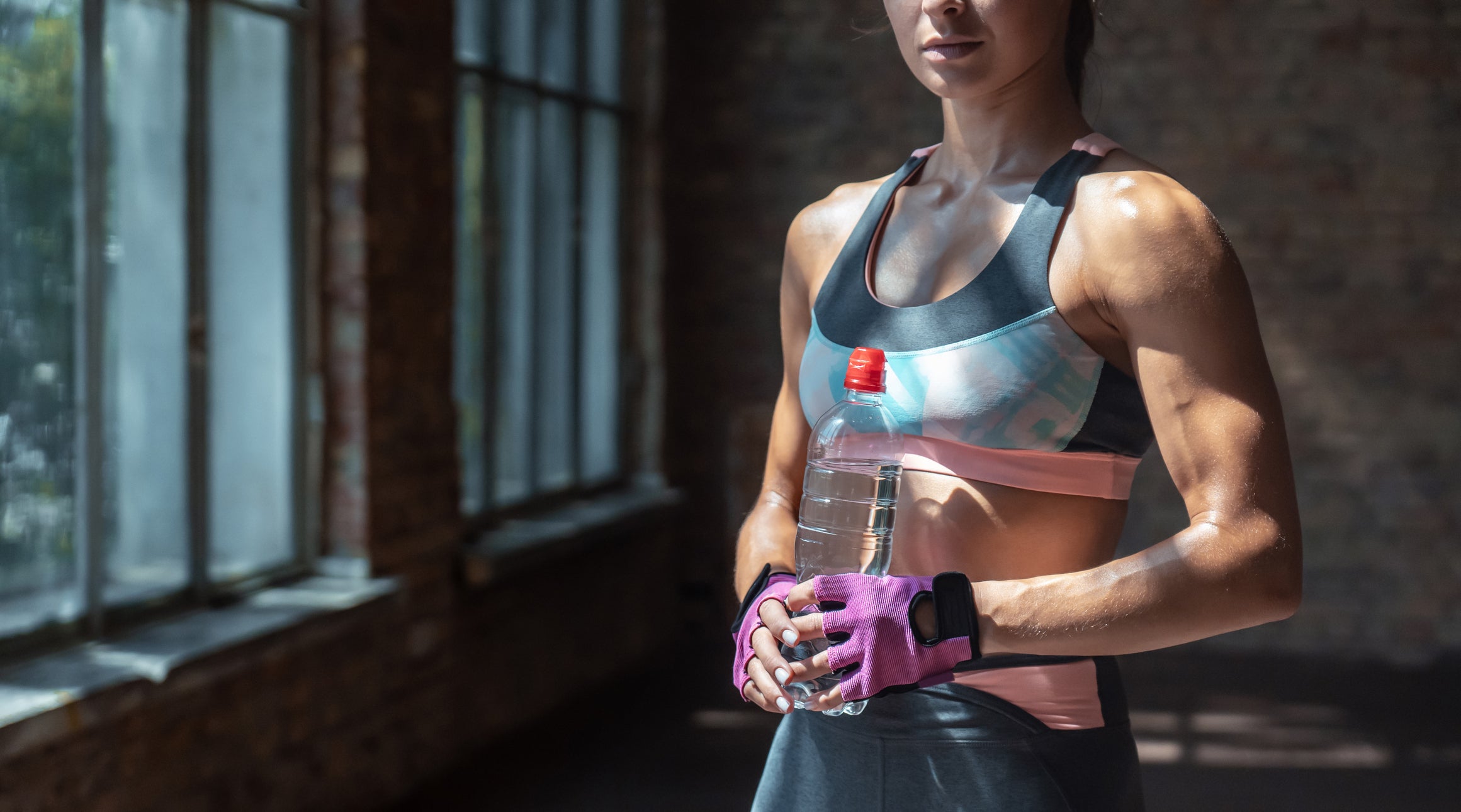 Woman in athletic wear holding a water bottle in a dimly lit room.